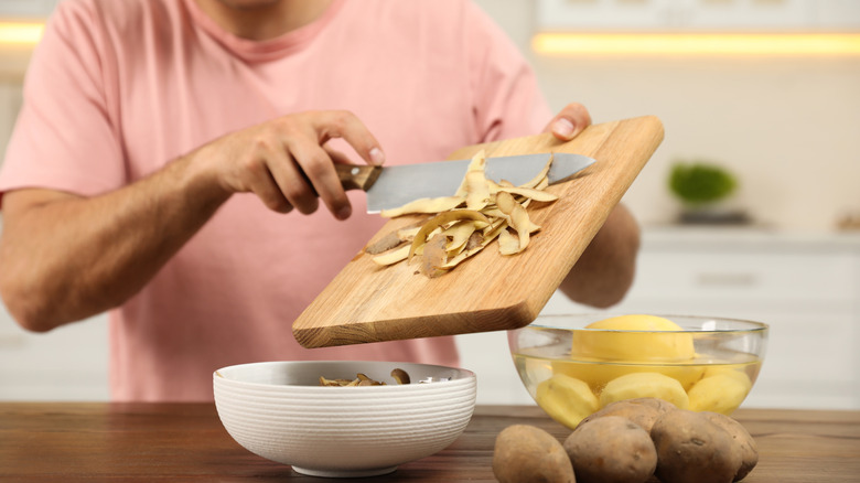 person using knife to scrape potato skins off cutting board