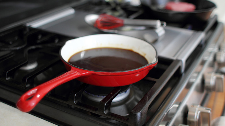 An enameled pan on a stove filled with dark liquid