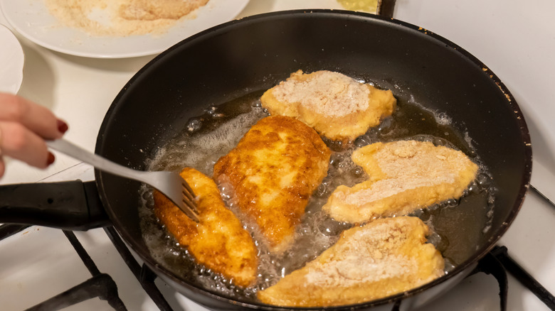 Breaded meat cutlets frying in hot oil in a pan on gas stove