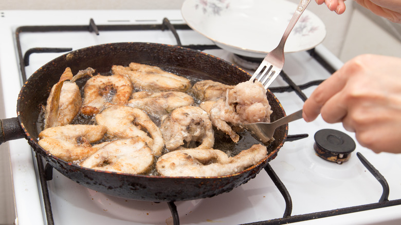 A pan full of fish is frying on a stove