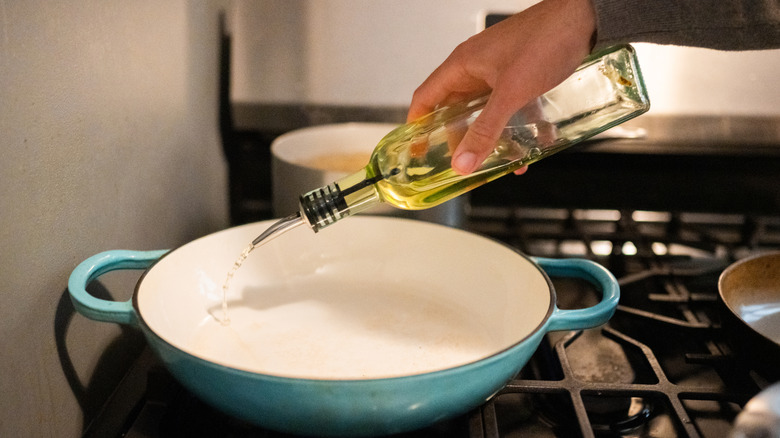 Close-up of a hand pouring olive oil into a pan