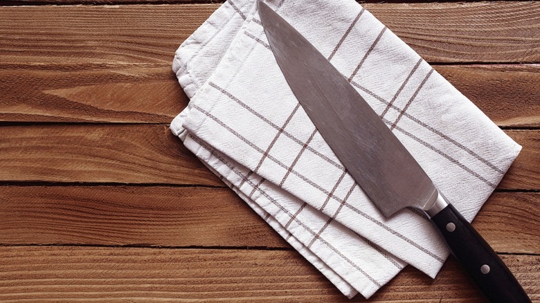 A chef's knife laid out on a white cloth on a wooden background