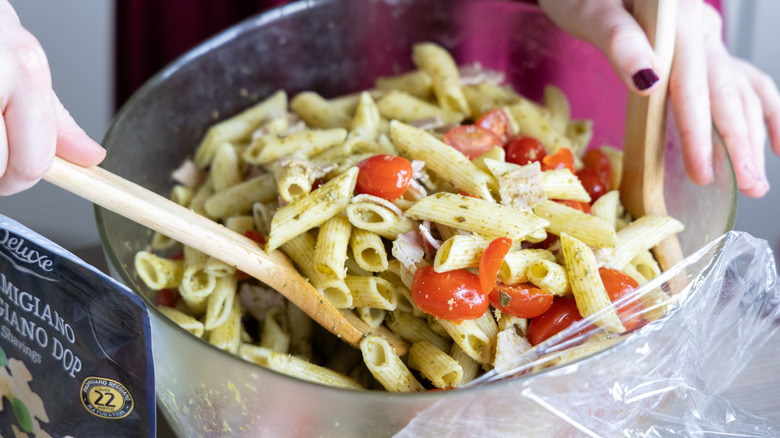 Pasta salad being tossed with wooden tongs