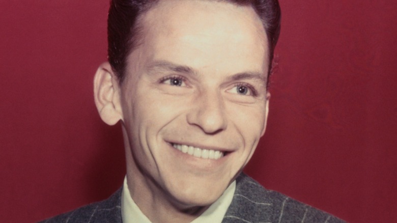 closeup of a young Frank Sinatra smiling in front of a red background