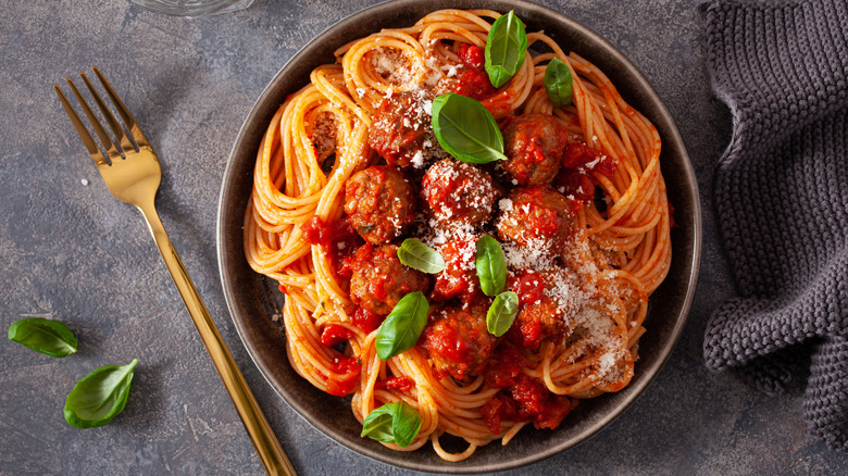 spaghetti and meatballs in a gray bowl next to fork and mint leaves
