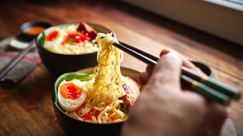 A person using chopsticks to eat a bowl of ramen.