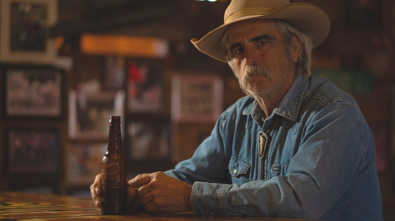 Man wearing a cowboy hat sitting with a drink at a rustic bar