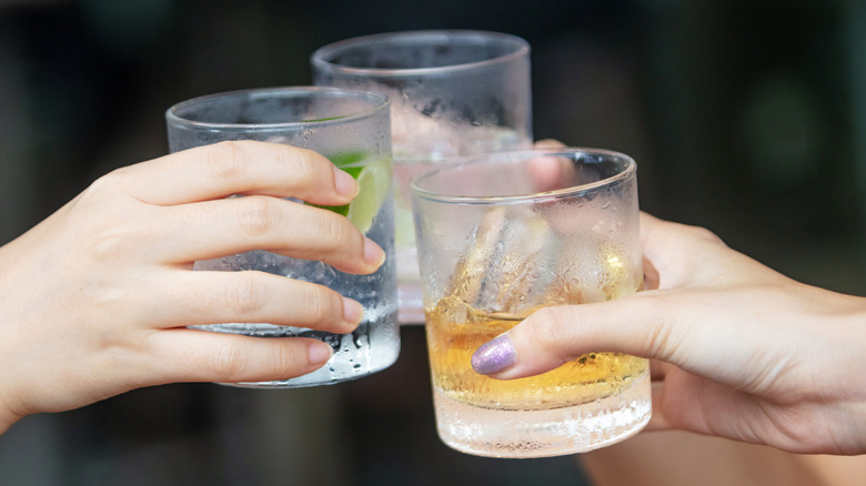 Cheersing with three short glasses filled with clear liquor on the rocks