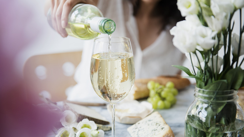 A woman pour some light white wine into a glass.