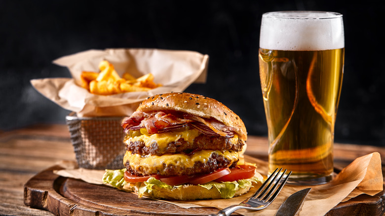 Double cheeseburger alongside pint of beer and French fries
