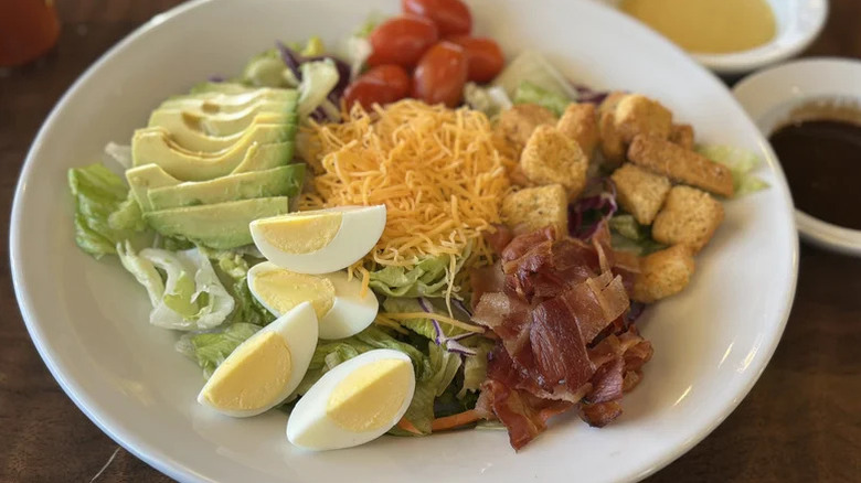 A Cobb salad in a bowl at Denny's with salad dressing in the background.