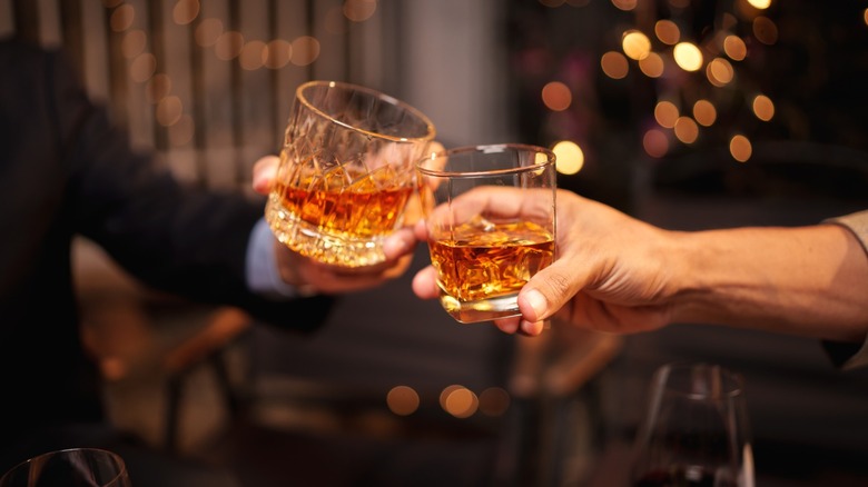 Two people clink glasses of whiskey at a bar