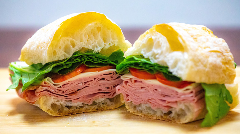 Bologna sandwich on ciabatta bread on a light wooden table.