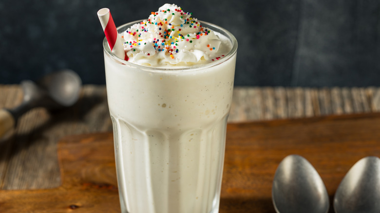 A milkshake topped with whipped cream, rainbow sprinkles, and a straw