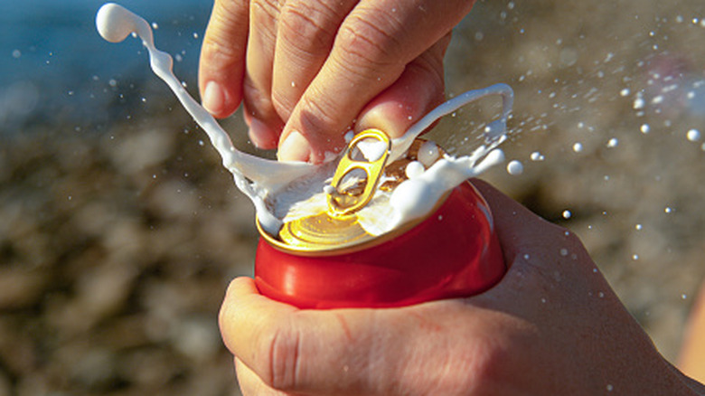Hand opening can of beer spewing foam