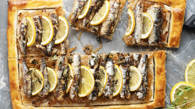 Sardines on a rectangular pizza with lemon wedges on top