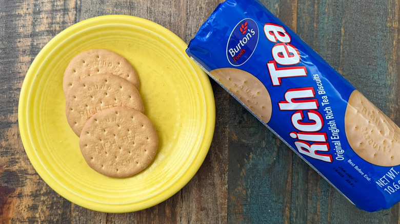 Three Burton's Rich Tea Biscuits on a yellow plate next to an unopened package.