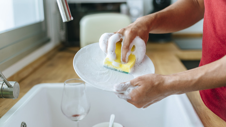 Someone using a soapy sponge to wash dishes