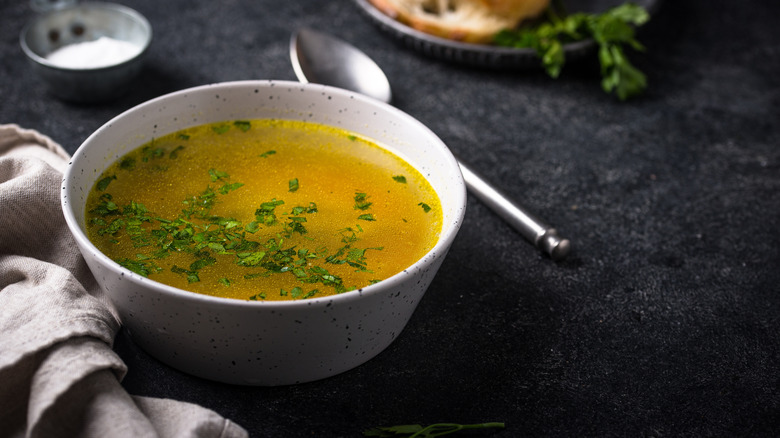 Chicken broth with parsley served in a white bowl with a spoon on the side.