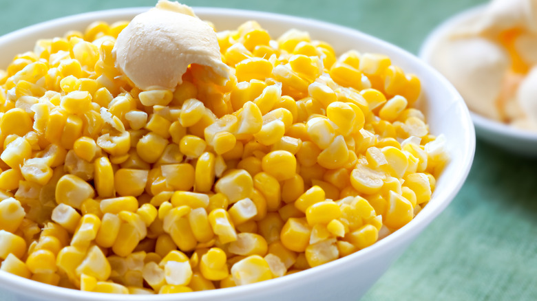 Cooked corn in a white bowl with a curl of butter on top