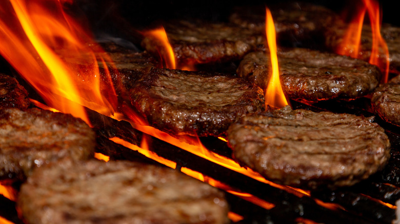 Burger patties cooking on a grill with fire bursting through the grates