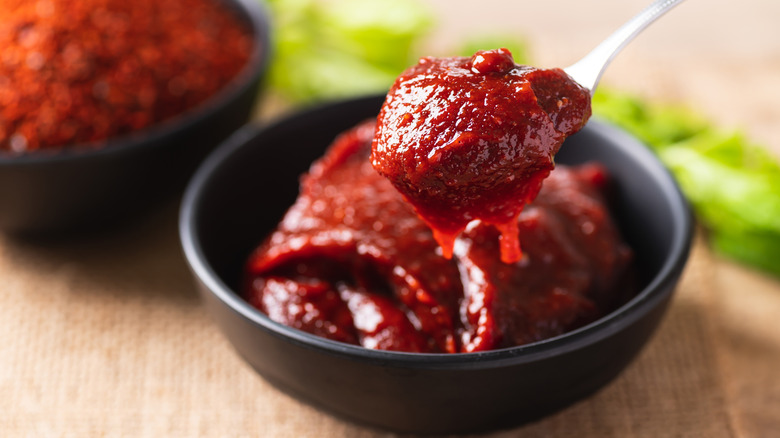 A small black bowl of gochujang paste with a spoon scooping some up.
