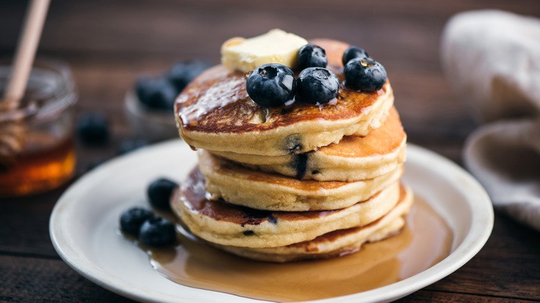 A stack of thick and fluffy pancakes topped with butter and blueberries.