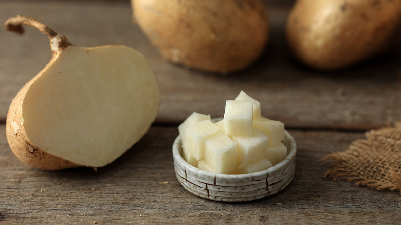 Jicama cut in half with a bowl of diced jicama on a wooden table