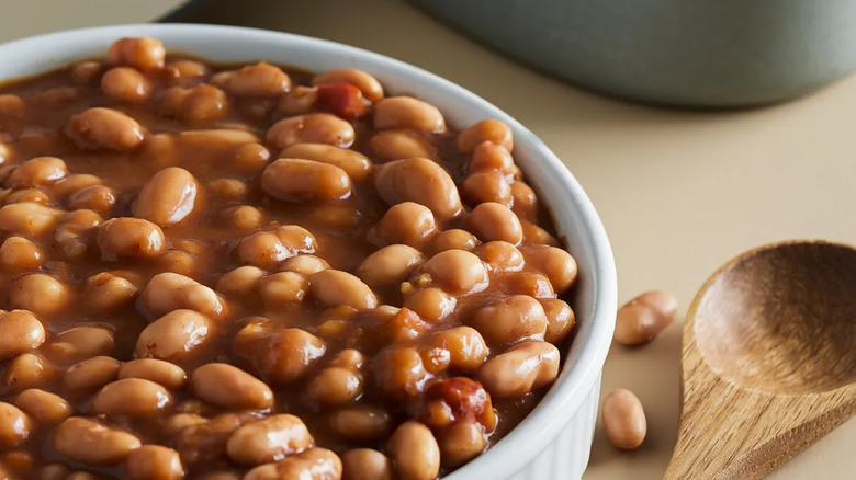 Close up of a dish of baked beans alongside a wooden spoon