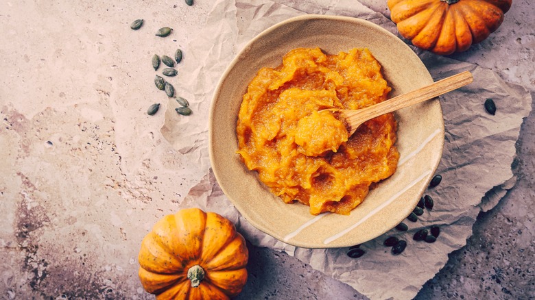 A bowl of pumpkin puree with a wooden spoon and two small decorative gourds