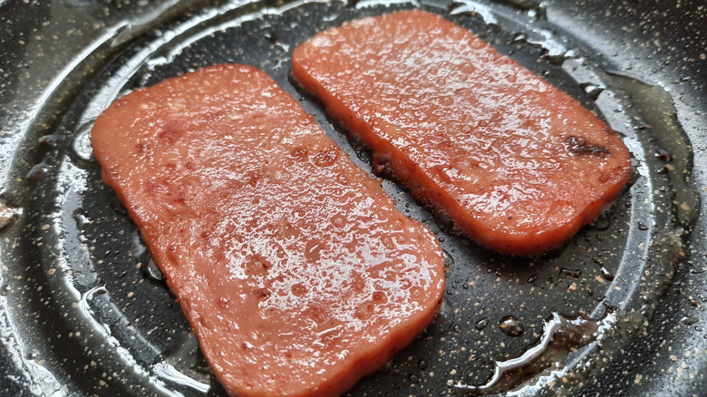 two pieces of Spam frying in a skillet