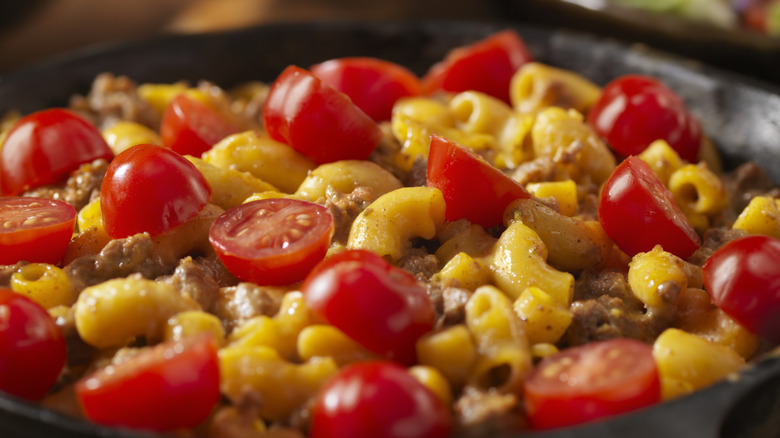 A cast iron skillet close up of hamburger helper with sliced cherry tomatoes