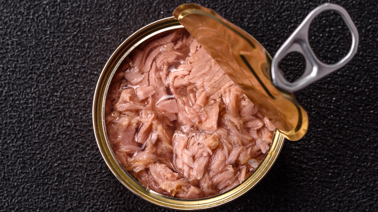 An open can of tuna on a black surface.
