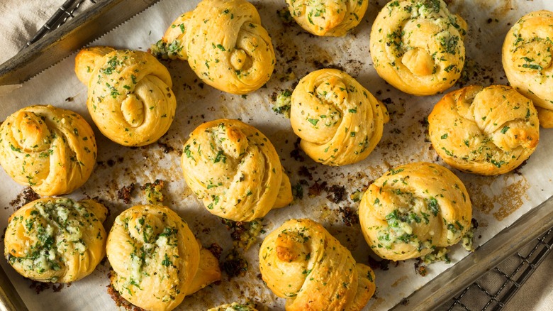 Buttery garlic knots with herbs on baking sheet