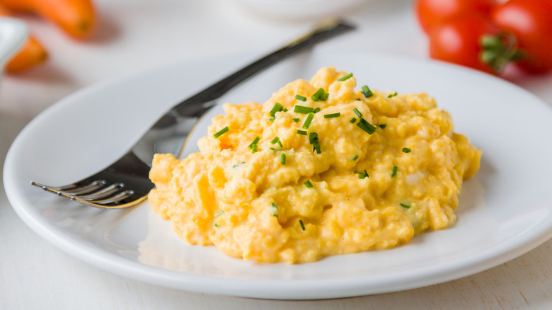 Fresh scrambled eggs on white plate on breakfast table.