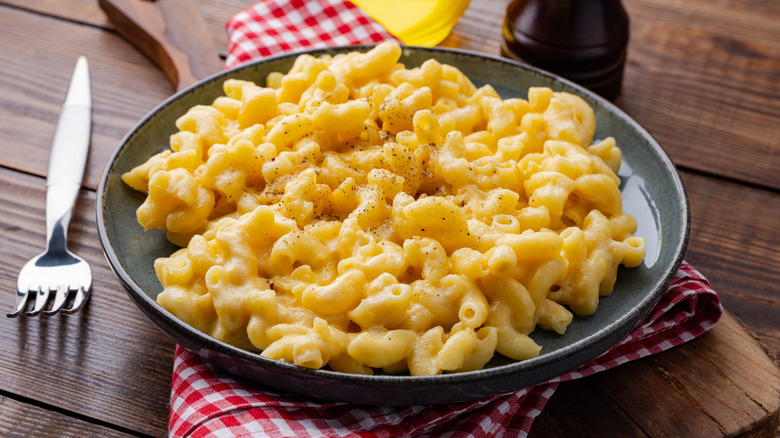 Delicious mac and cheese served in a plate on wooden table, with a table cloth and chopping board below and a fork on the side.