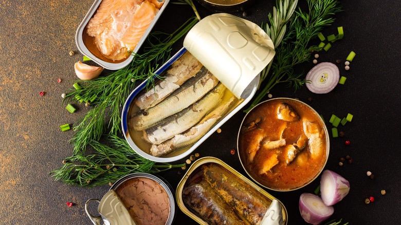 Various types of opened canned seafood surrounded by herbs