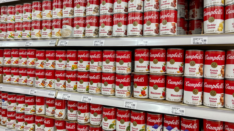 A store shelf stacked full of cans of different Campbell's soup flavors