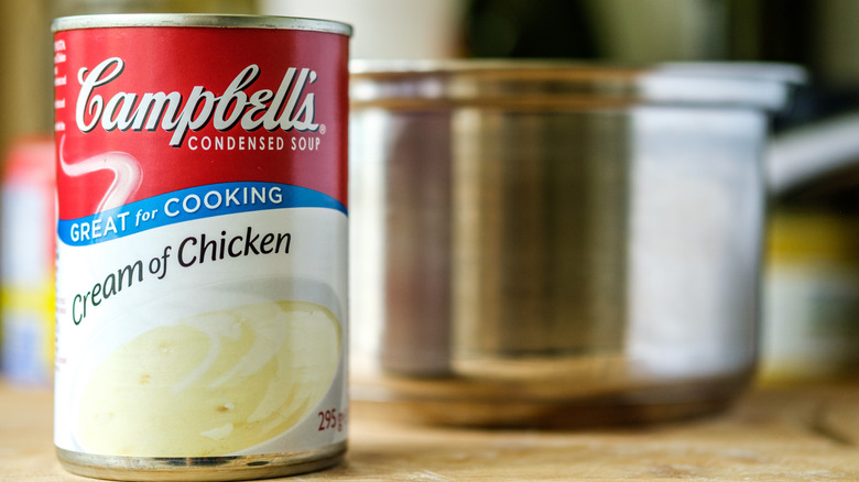 A can of Campbell's Cream of Chicken soup beside a large metal cooking pot.
