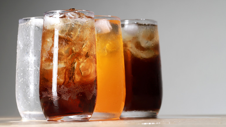 Four glasses of carbonated beverages with ice against a grey background