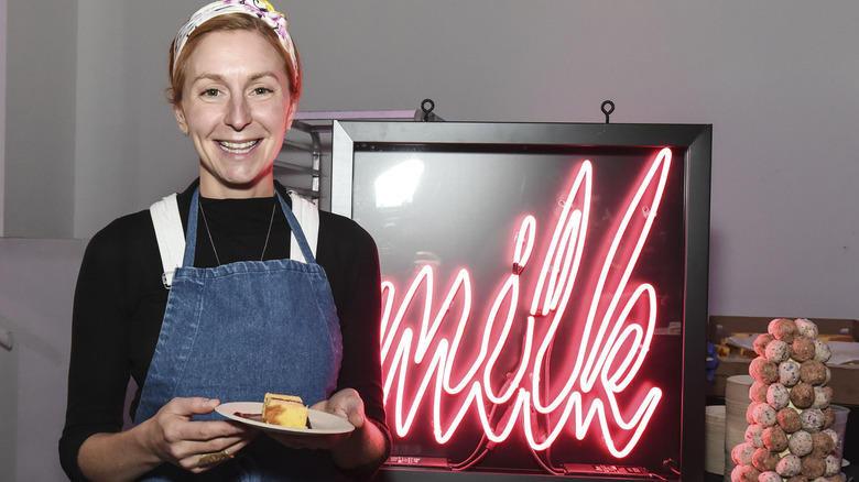 Christina Tosi holdin a dessert in front of Milk neon