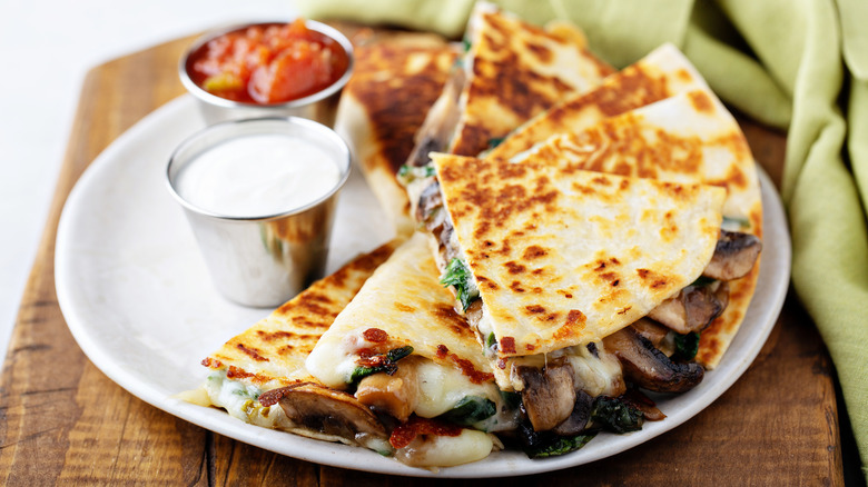 Sliced quesadilla on a plate with ramekins of sour cream and salsa