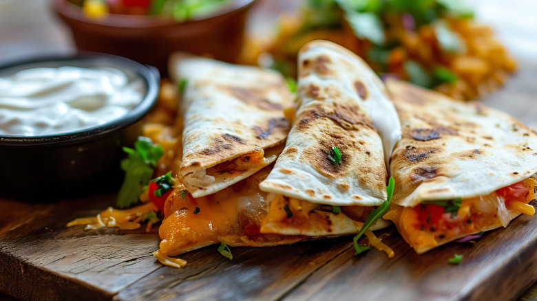 Quesadillas on a wooden cutting board with a ramekin of sour cream