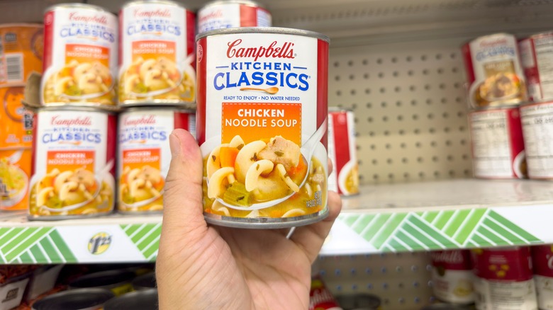 hand holds up canned chicken noodle soup in store