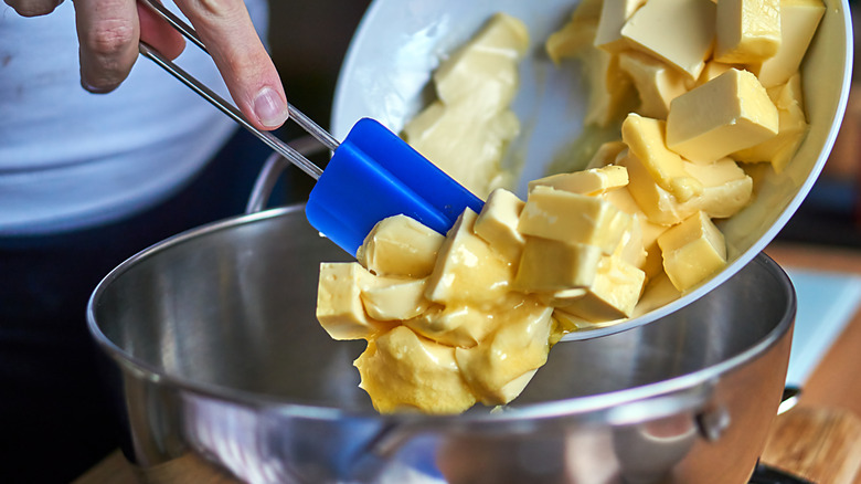 hand scraping butter chunks into a bowl with a blue spatula