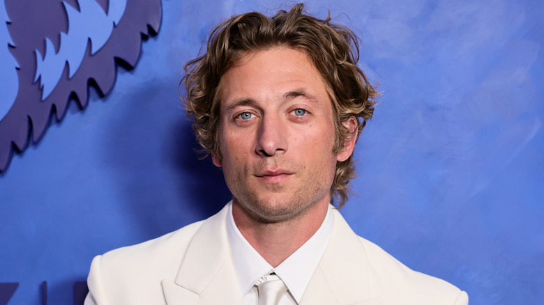 Actor Jeremy Allen White stands in a white suit against a blue wall.
