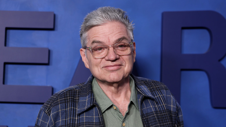 Actor Oliver Platt stands in front of a blue wall.
