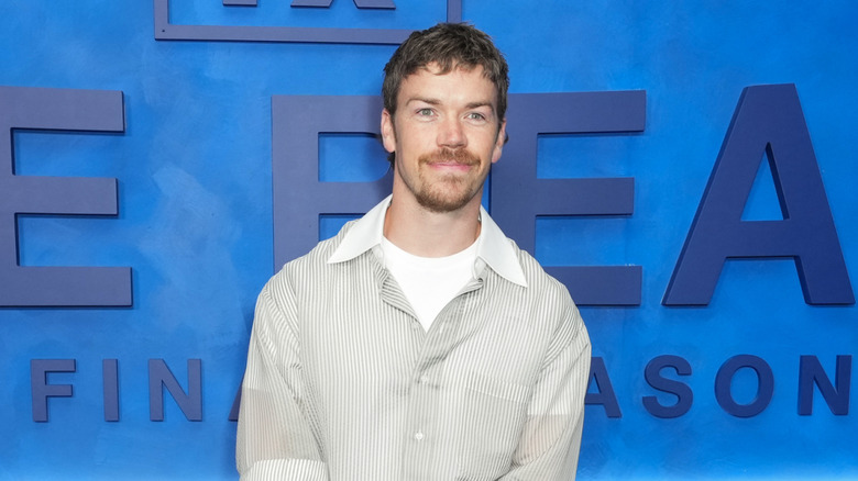 Actor Will Poulter stands in front of a blue wall.