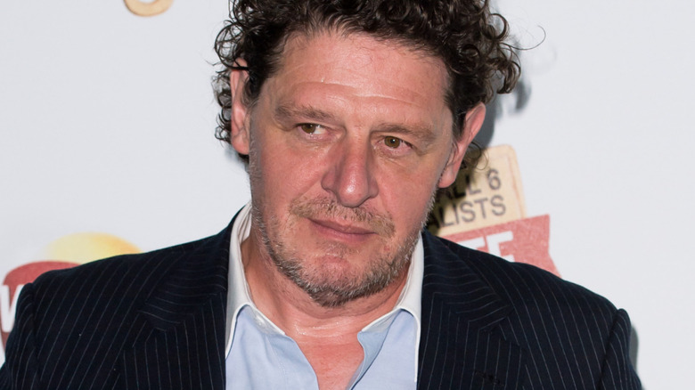 Marco Pierre White wears a suit jacket and blue shirt at an event