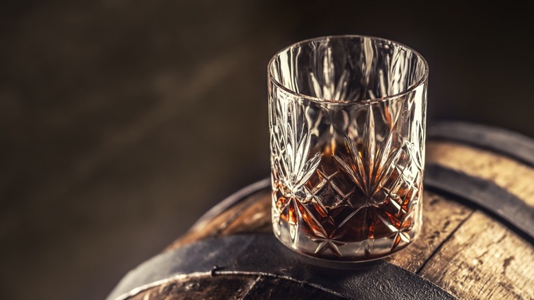 A glass of bourbon sitting atop an oak barrel.